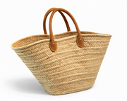 Woven straw tote bag with brown leather handles on a white background