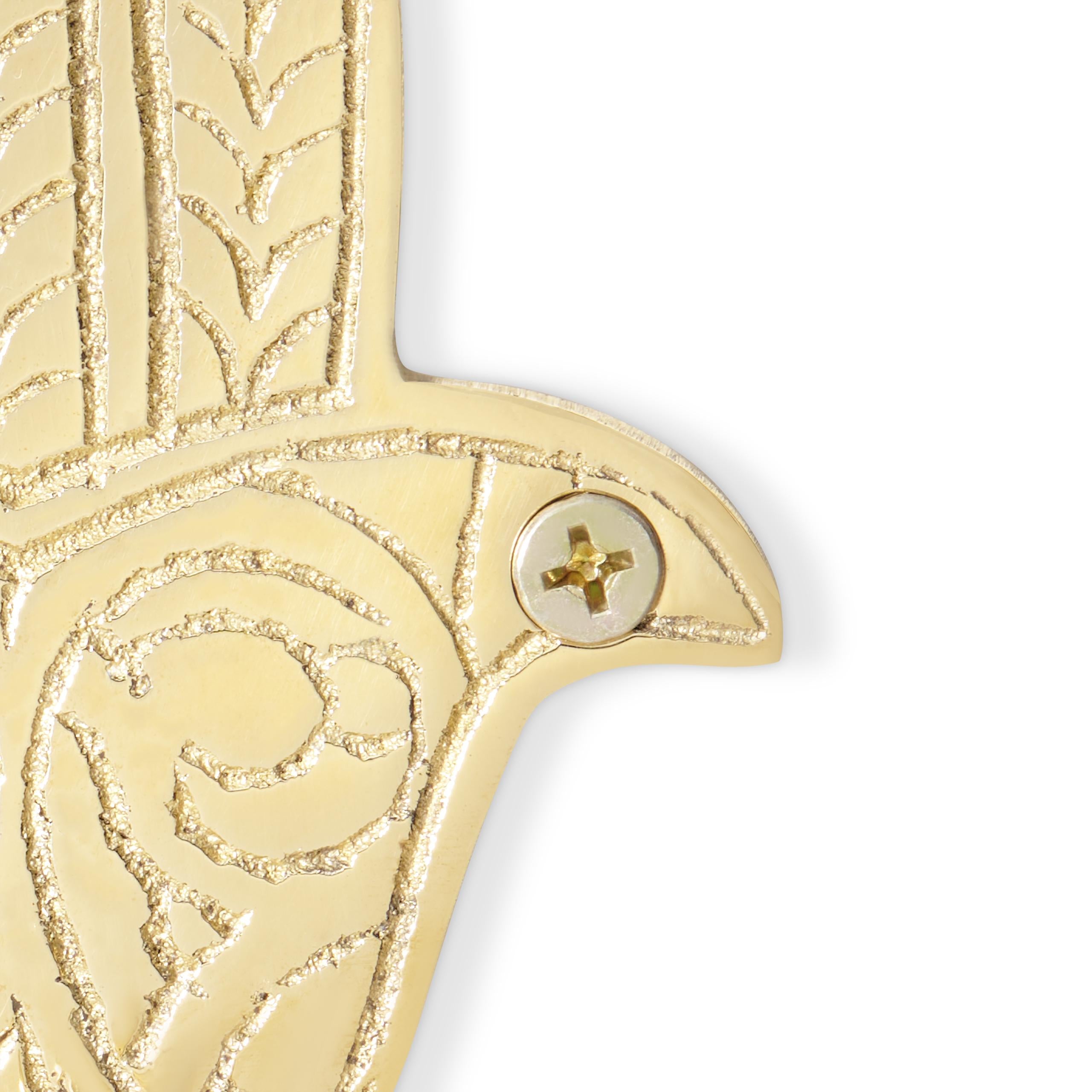 close up on details of a handmade brass wall hook with intricate patterns on a white background