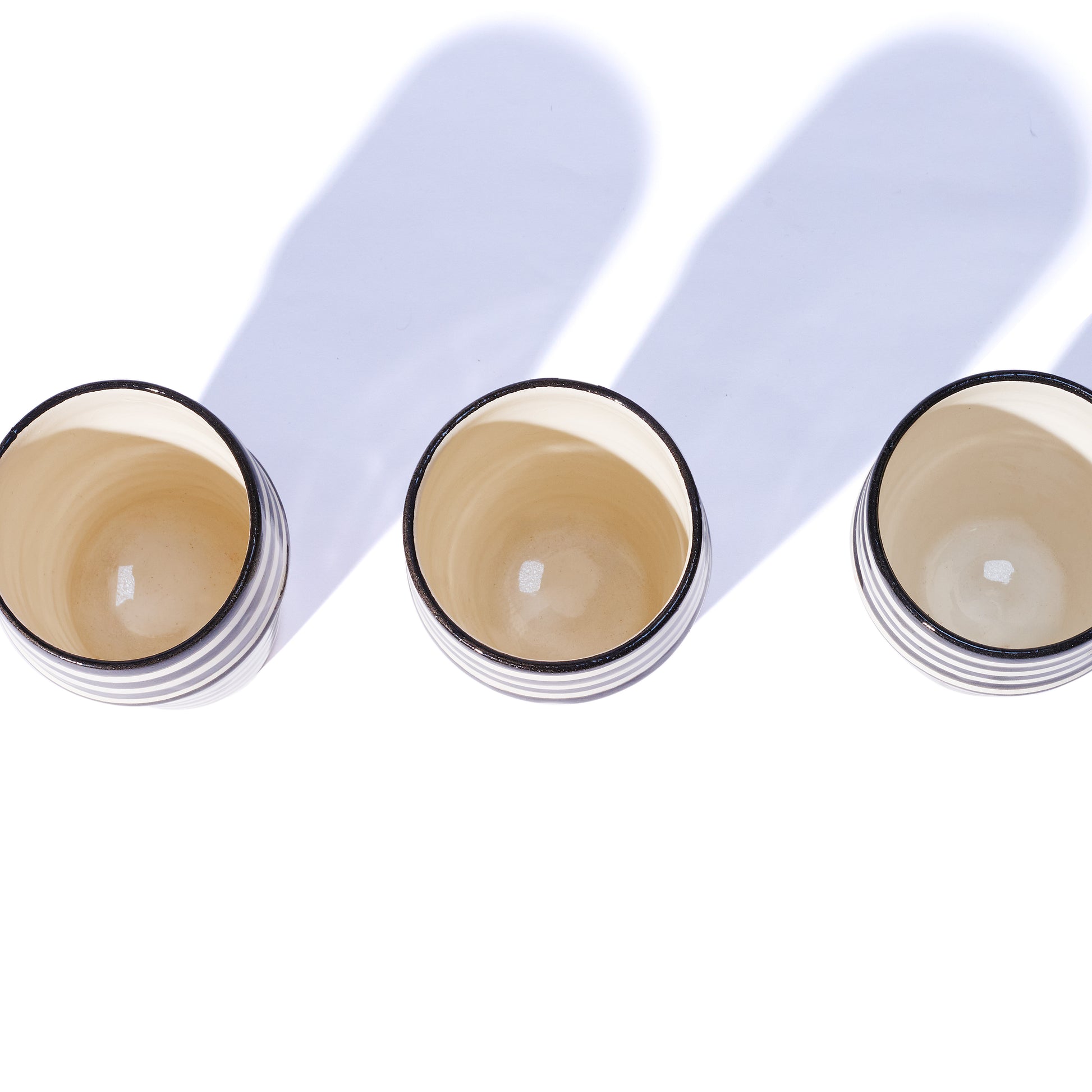 Overhead shot of three ceramic cups with beige cream inside on a white background