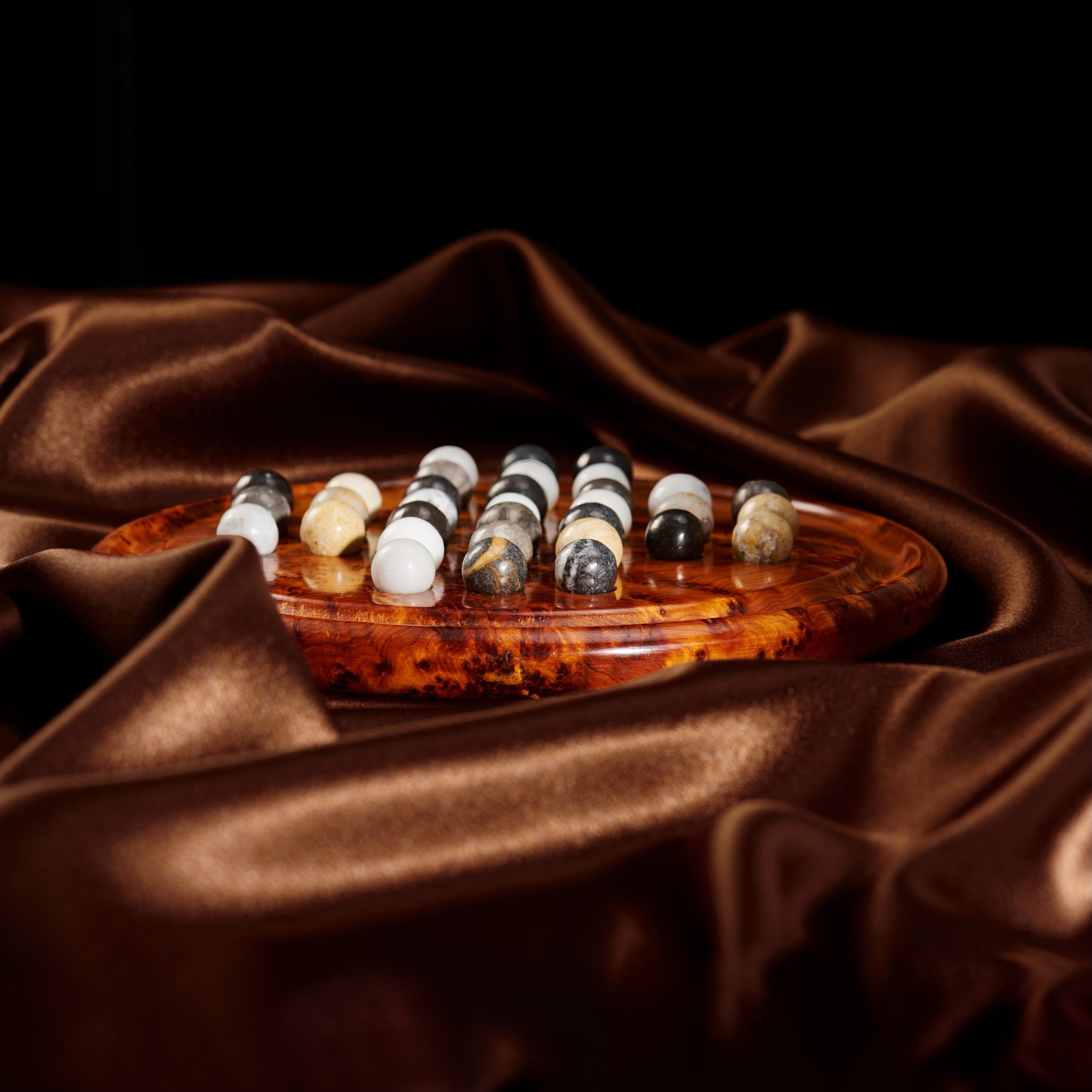 Set of marble balls on a wooden solitaire board with a brown fabric background