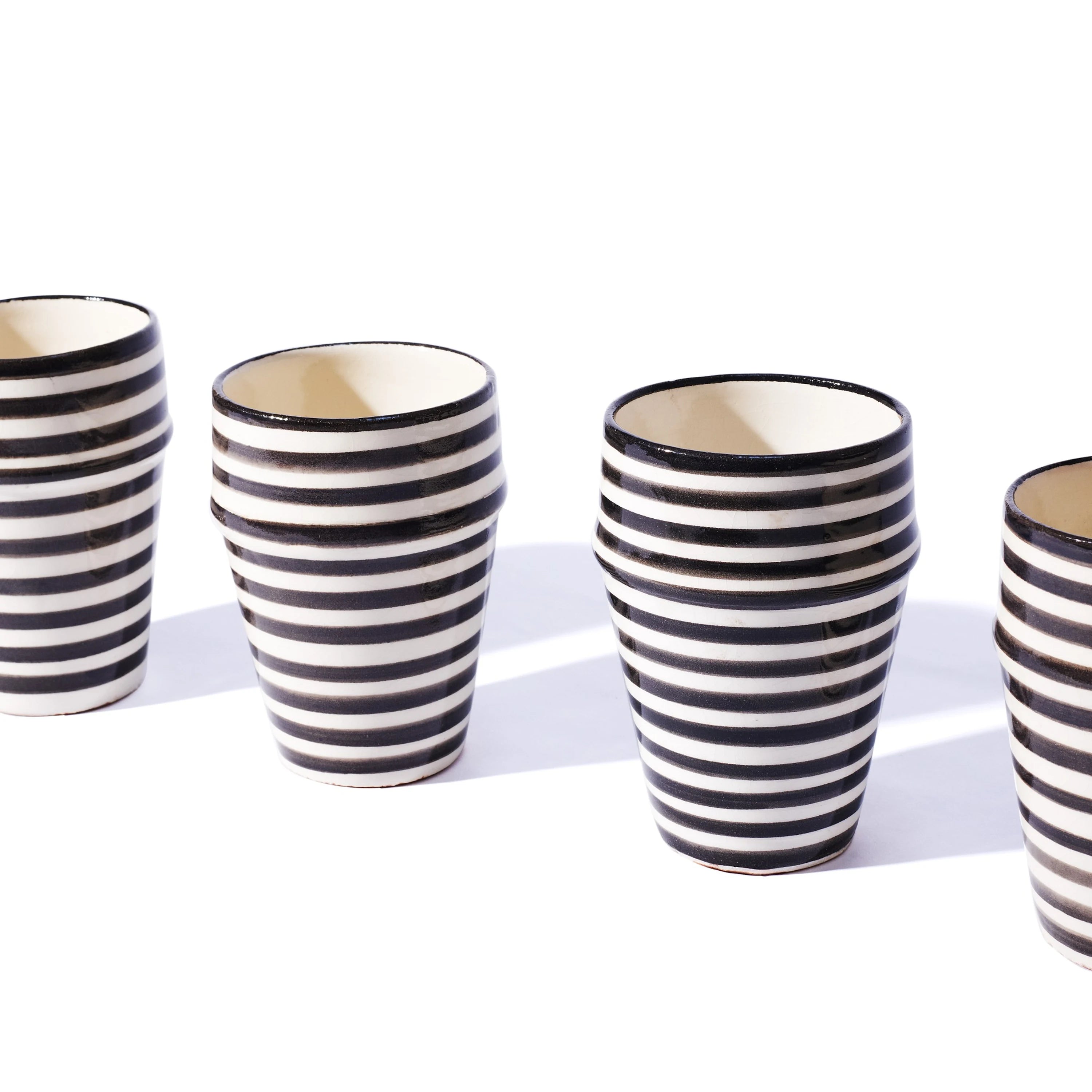 Set of four black and white striped ceramic cups on a white background