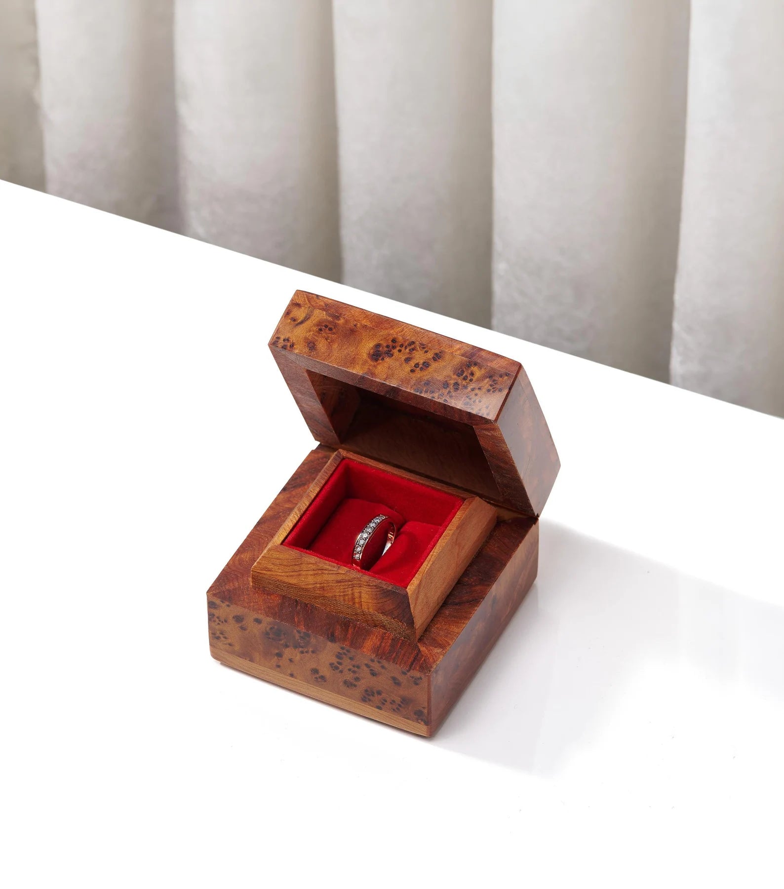 Wooden ring box with a red interior containing a ring on a white surface.